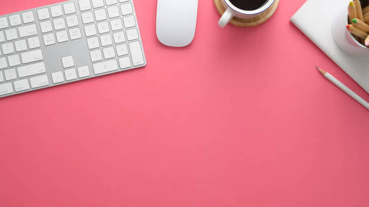 在粉红色的桌子背景上，用电脑文具电脑文具咖啡杯和复印空间拍摄的时尚工作空间