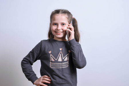 一个白人小女孩的肖像在灰色背景下通过电话交谈