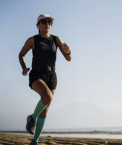 户外健身生活方式图片年轻迷人的运动妇女穿着压缩跑步袜在海滩上慢跑