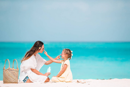 年轻的母亲在海滩上给女儿涂防晒霜。防晒