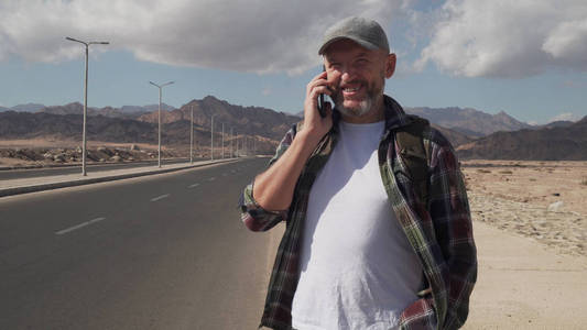 站在沙漠中的一条路上，英俊的老年男子站在手机旁聊天