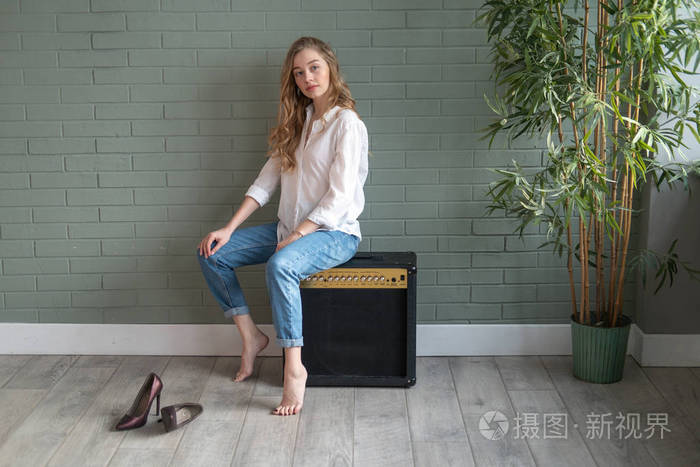 年轻漂亮的女人光着脚坐在低音炮旁的绿色植物旁