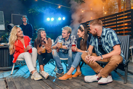 周末晚上,四个兴高采烈的年轻人坐在后院的椅子上聊天,喝着啤酒.