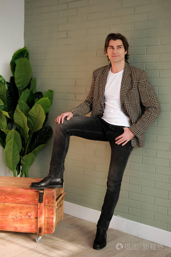 高大英俊的男人站在灰色的墙壁和木箱旁照片-正版商