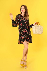 Young woman wearing floral print dress with straw bag on yellow 