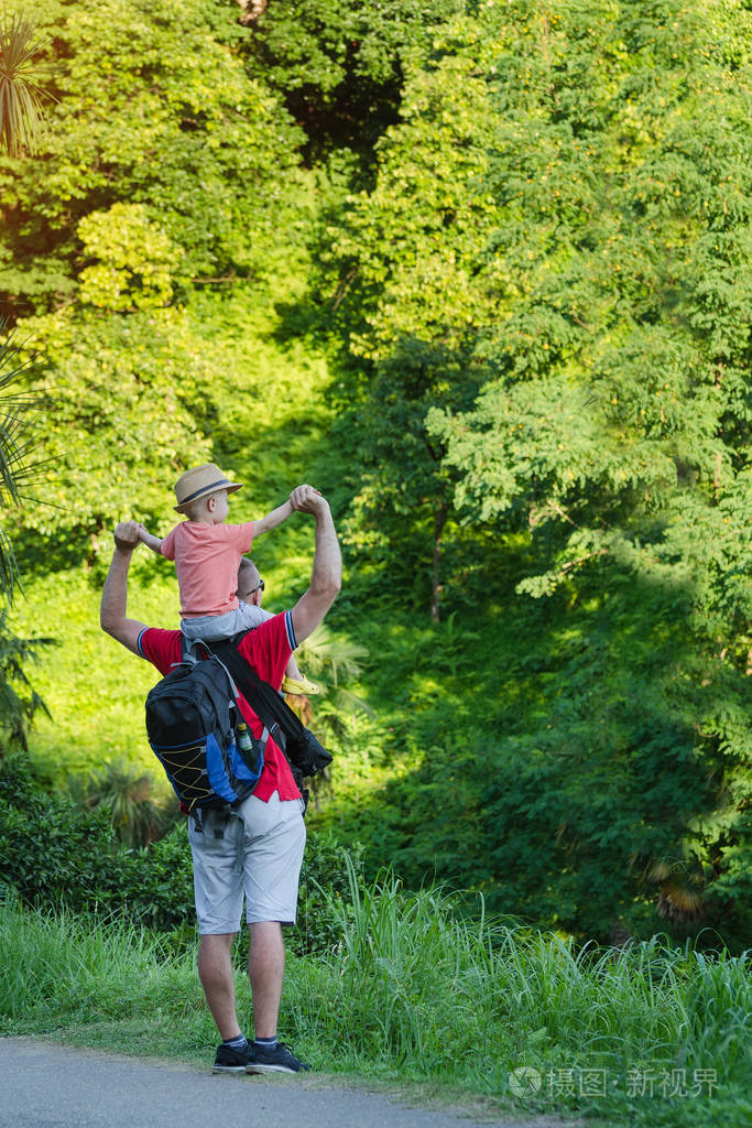 儿子坐在父亲的肩膀上爸爸和儿子在夏日公园散步垂直框架