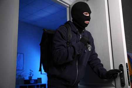 小偷拿着手电筒在夜间闯入房子照片