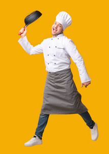 黄色背景下滑稽的厨师跳着和煎锅摆姿势