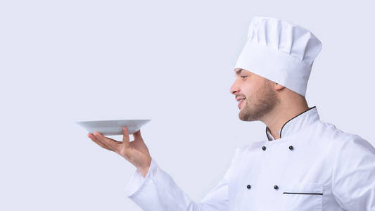 厨师拿着盘子在白色背景上端着看不见的菜，侧视