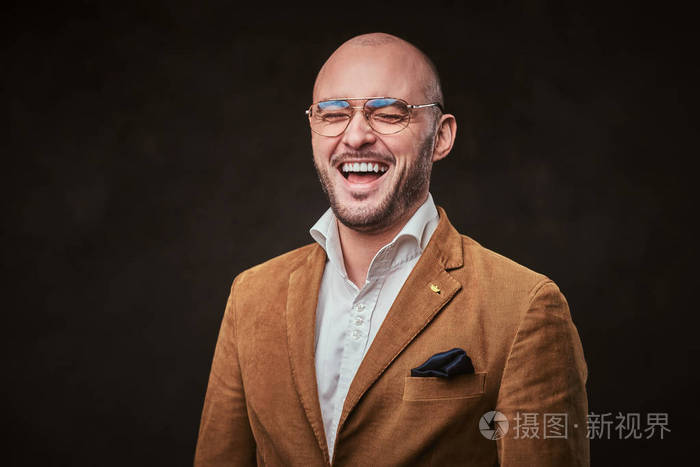 成功和微笑的光头商人穿着时髦的天鹅绒夹克白衬衫戴着眼镜在工作室里