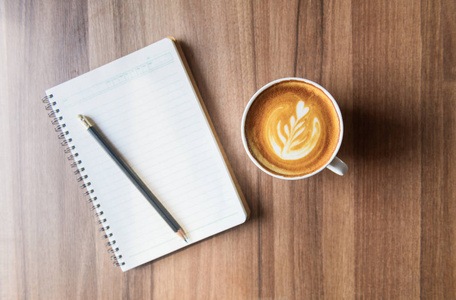 cup of latte art coffee with blank notebook and pencil 