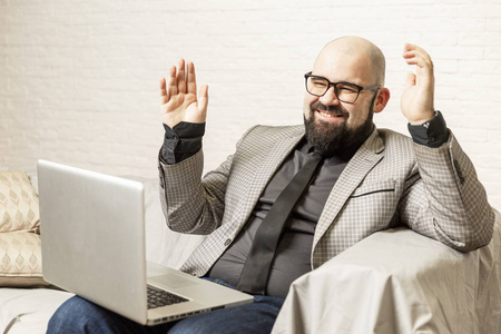 一个戴眼镜的秃头男人坐在沙发上用笔记本电脑。写博客和辅导。