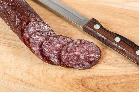 Sliced salami sausage and knife on wooden board 