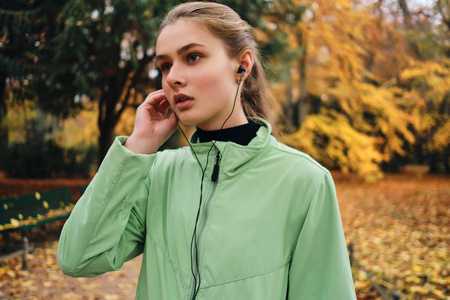 秋日公园运动女孩戴着耳机听音乐的肖像照片