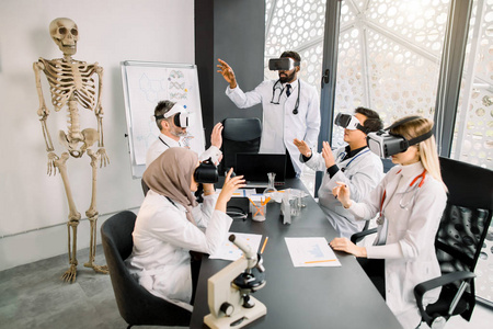 在现代实验室里，由教授带着虚拟现实眼镜学习医学或科学项目的多民族学生群体。医学研究，化学，科学，虚拟现实概念