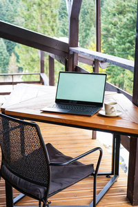 露台上的木制桌子上放着一个杯子的笔记本电脑，特写。早上好概念。文本的位置。
