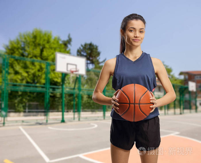 在室外篮球场上拿着篮球的年轻女子