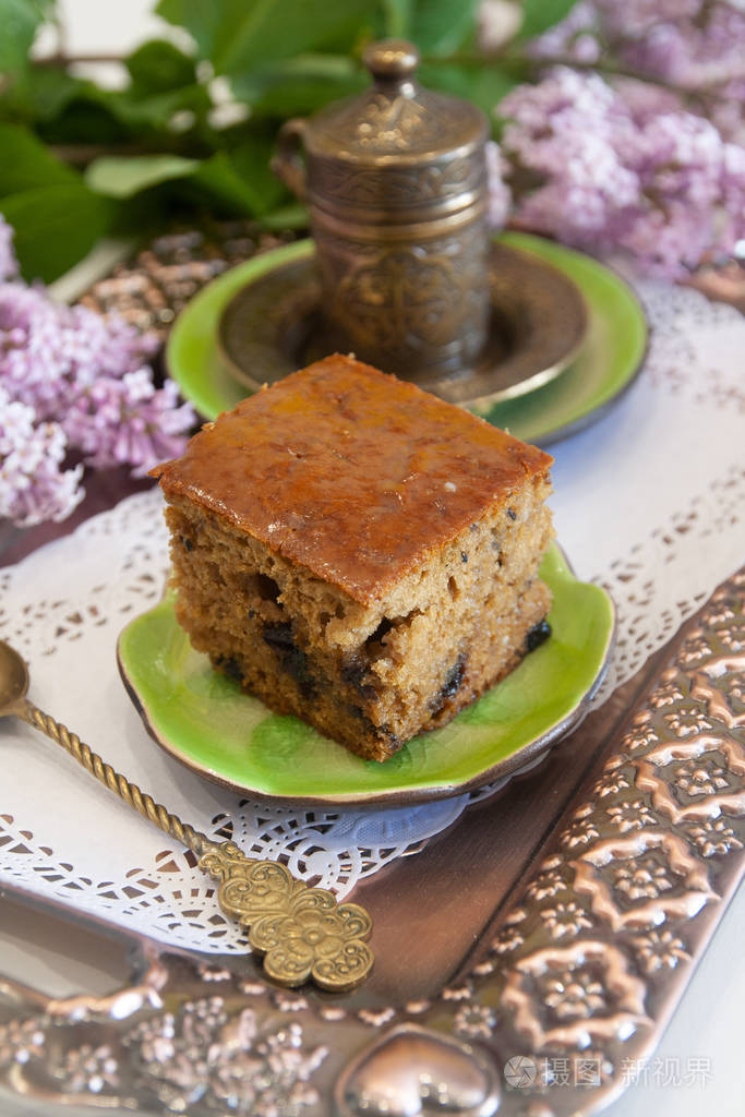 一片甜棕色的黑加仑子蛋糕在一个绿色的陶瓷盘子金属托盘咖啡杯精致的