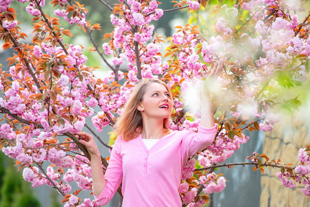 金发女子在樱花盛开的樱花园里尽情享受。阳光明媚的春天。快乐的女孩在春暖花开的花园里度过时光。