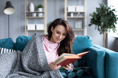 Beautiful smiling woman reading book on a cozy sofa at home. 