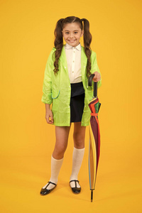可爱实用的风格。快乐的小女孩拿着黄色背景的优雅的手杖。小孩子穿着雨天装微笑。雨季流行款式