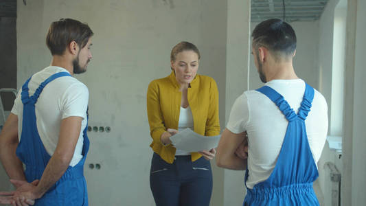 Woman with a drawing talks to repairmen 