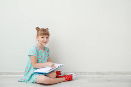 可爱的小女孩拿着书坐在白墙上