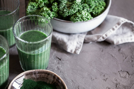一种健康的素食主义者在黑暗的背景下喝含有螺旋藻的绿色甘蓝冰沙