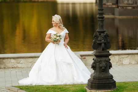 长发的年轻新娘手持结婚花束的肖像包括白玫瑰和其他鲜花。漂亮的白色结婚礼服。湖景美女