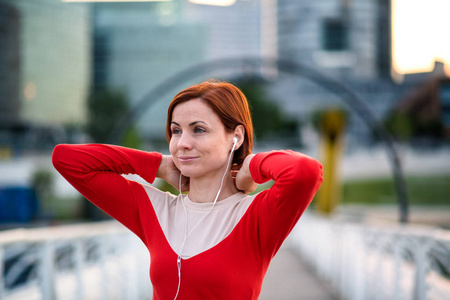 城市中戴着耳机的年轻女子跑步者的正视图，休息。