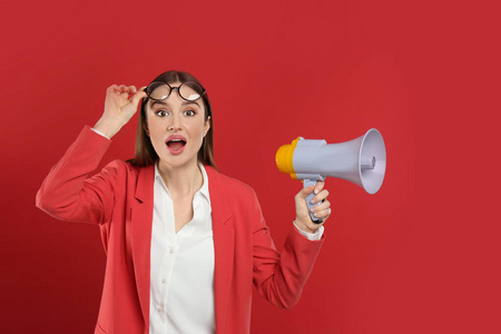 Emotional young woman with megaphone on red background
