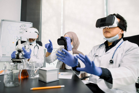 科学家团队，亚裔和高加索男性，阿拉伯女性使用虚拟现实护目镜在实验室进行科学研究，手势手势。医学，遗传学，药学，生物技术概念