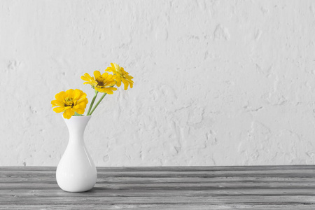 yellow zinnia in white vase on wooden table 