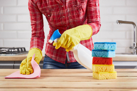 穿着黄色橡胶防护手套的女士用喷雾器海绵和布清洁木制桌子，厨房背景