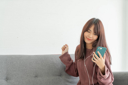 Asian woman using smartphone on grey sofa in living room 