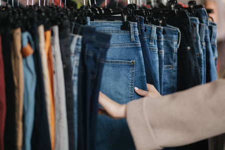 女人选择牛仔裤的特写镜头。在服装店里拿着牛仔裤的女人的手