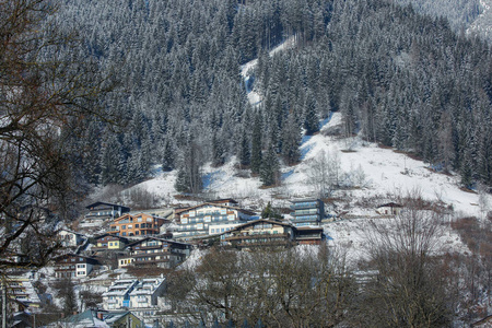 阿尔卑斯山的冬季山坡，阳光明媚的村舍积雪和森林