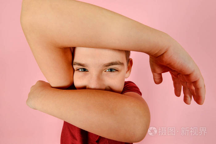 一个穿着酒红色t恤的有趣男孩用手托着他的头,粉色背景,一张几何扭曲