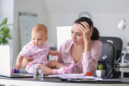 压力大的母亲带着孩子在办公室工作照片