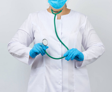 medic woman in a white coat and mask holds a green stethoscope 