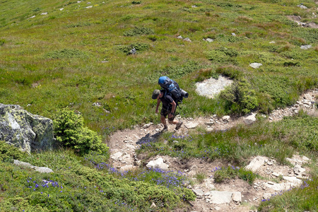 背着徒步旅行背包的游客沿着山路散步。说明健康生活方式的背景。