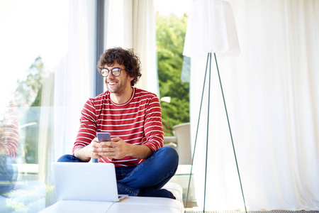 Happy young man daydreaming and text messaging while sitting at 