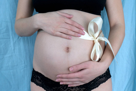 年轻漂亮的孕妇穿着黑色内衣，双手放在腹部，蓝色的丝带上。母性，怀孕概念