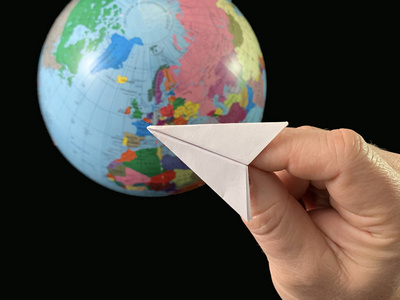 手上的纸平面背景是地球仪，黑色背景。飞机在世界各地飞行。一个人用手指着地球仪。概念旅游，旅游，
