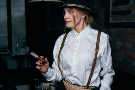 高级迷人的女流氓在餐厅黑暗的背景下抽雪茄照片