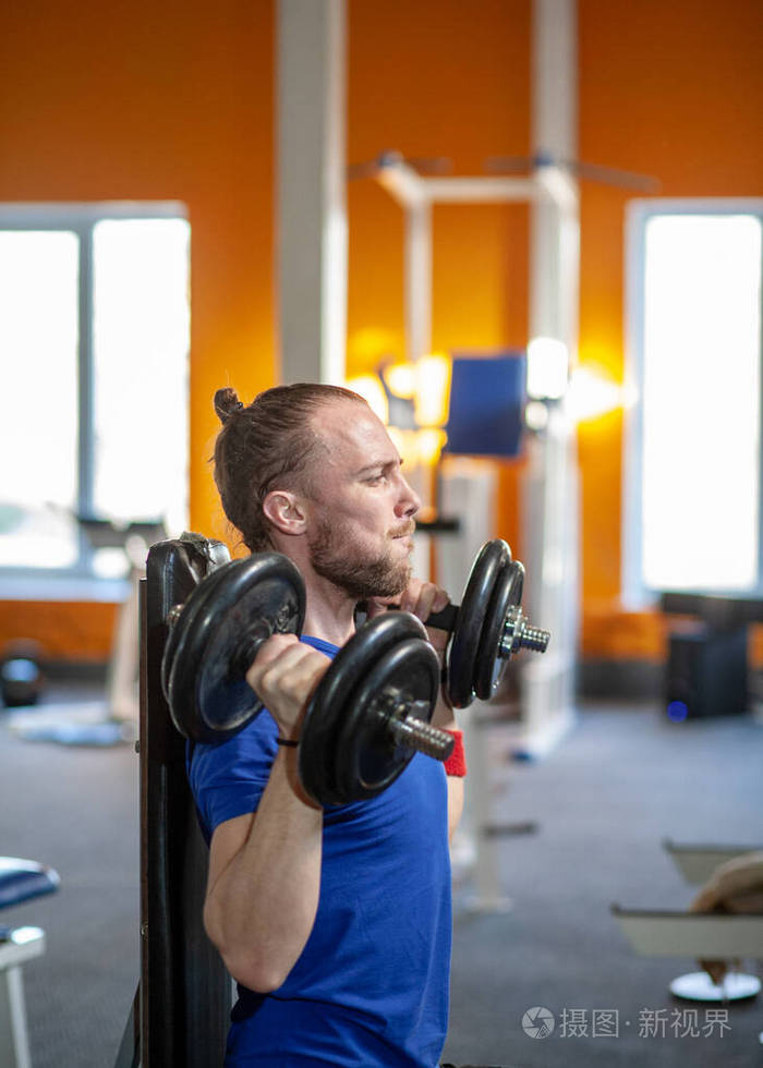 在体育俱乐部举重的强壮男子在健身房用哑铃练习肌肉帅气的健身教练在