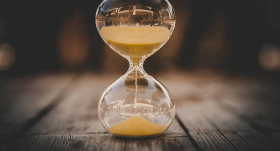 沙漏上落下的沙漏,在木质的背景上,夏日时光,时光流逝的概念照片