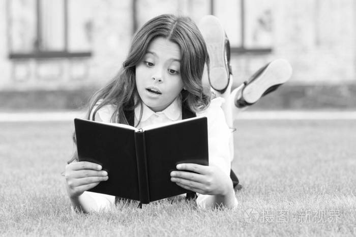 学习概念。课外阅读。可爱的小孩在户外看书。基础教育。可爱的小女孩学读书。女学生校服躺在草坪上放着最喜欢的书