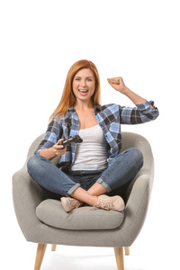 Emotional woman playing video game while sitting in armchair aga