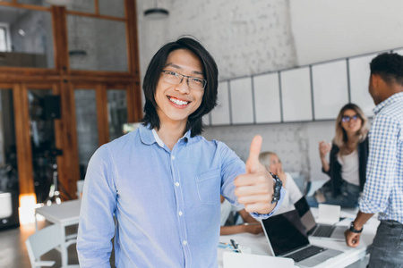 身着蓝色衬衫,戴着眼镜的中国上班族,微笑着,背景是笔记本电脑.照片